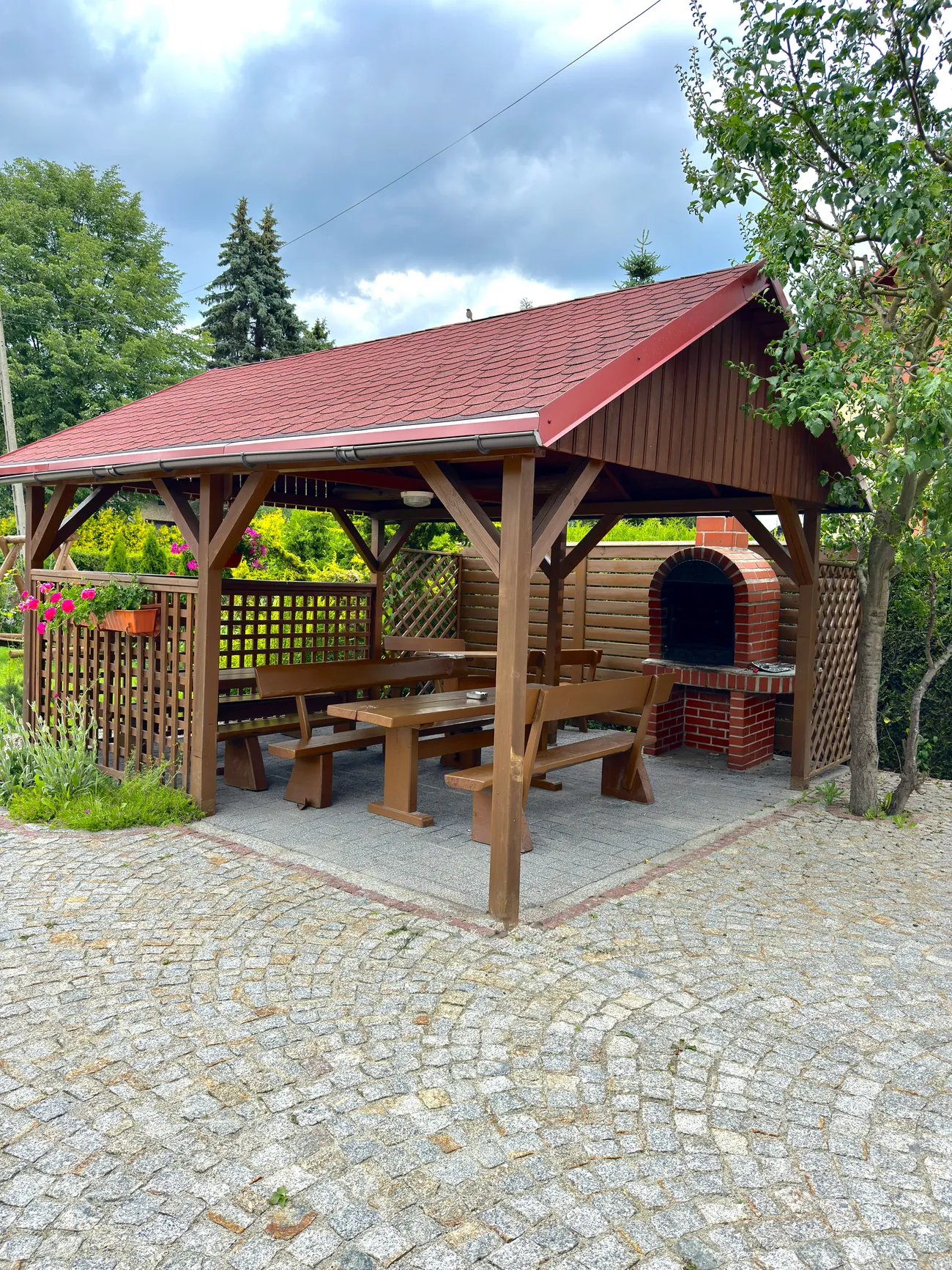 Drewniana altana ze stołami i murowanym grillem w ogrodzie
